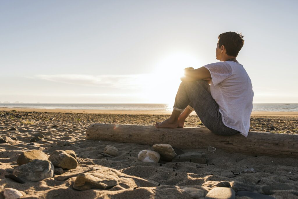 France, Bretagne, Crozon peninsula, woman sitting on beach at sunset